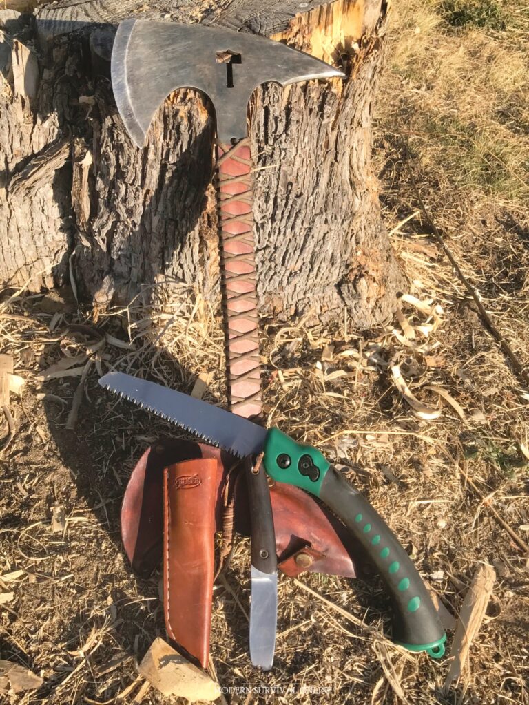 axe knife and folding saw next to tree trunk